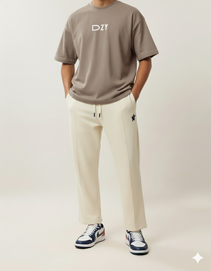 Person wearing a brown t-shirt with 'DZY' logo, beige pants, and black and white sneakers on a light background
