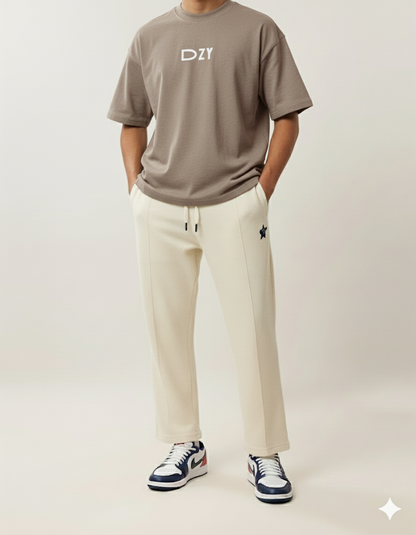 Person wearing a brown t-shirt with 'DZY' logo, beige pants, and black and white sneakers on a light background